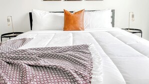 A neatly made bed with patterned bedding, a single brown pillow, and a white headboard. - Sleepover | Updated 1BR/1BA + Gym - Cincinnati (Cincinnati)