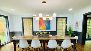 A dining room with a wooden table and white chairs, a chandelier, and a colorful abstract painting on the wall. - Horton House SLEEPS 16, no pets or unapproved parties (Monroe)
