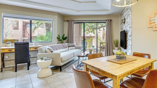 A modern living room with a sofa, dining table, and chairs. There is a TV mounted on the wall and a window providing a view of the outdoors. - 3 Mi to Sabino Canyon: Condo w/ Resort Perks! (Tucson)