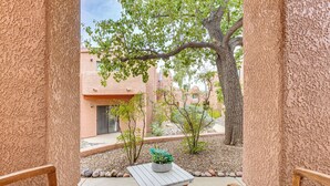 An outdoor patio with a wooden table and two chairs, a potted plant, and a view of a building with a stucco exterior. - 3 Mi to Sabino Canyon: Condo w/ Resort Perks! (Tucson)
