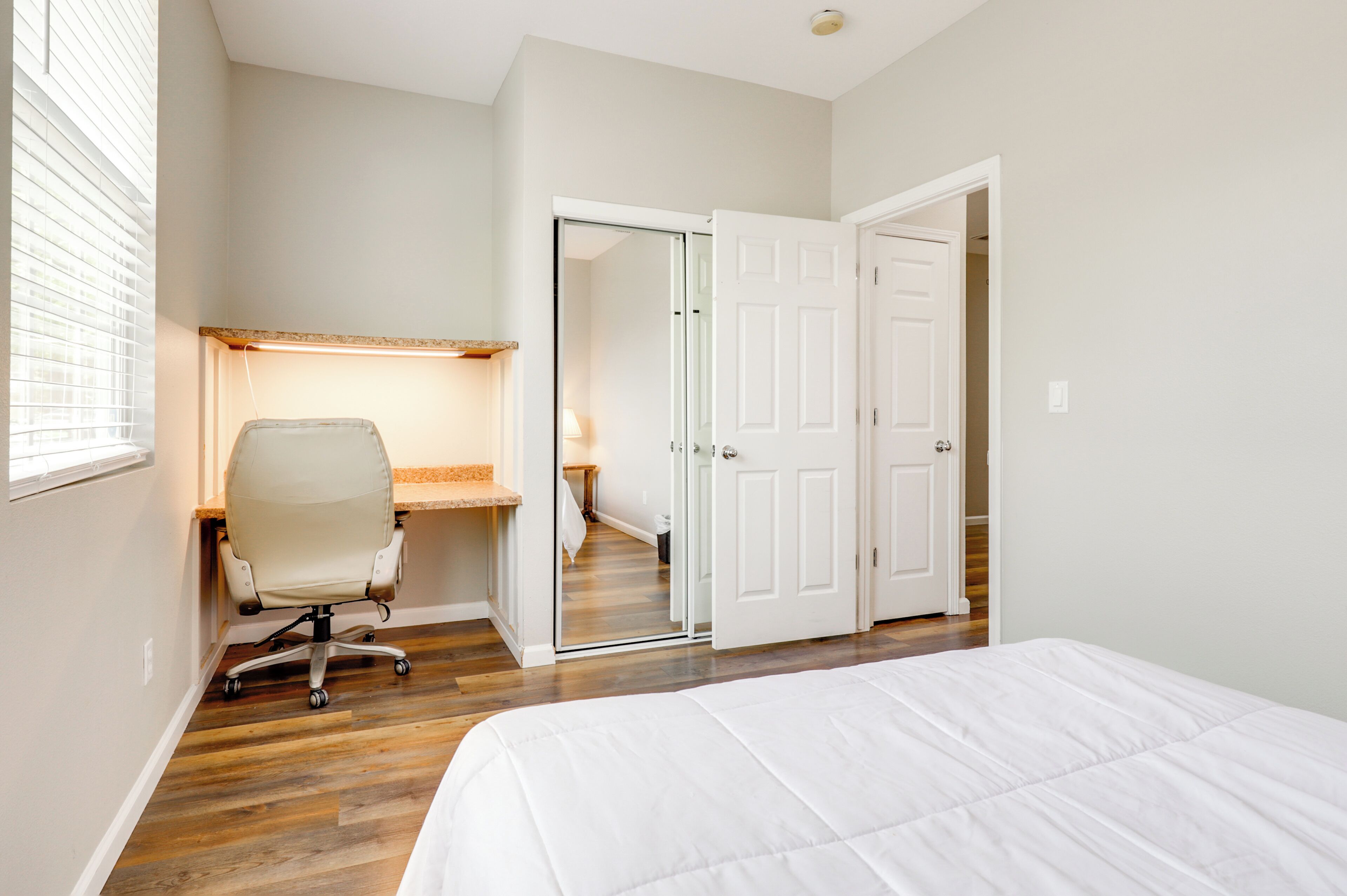 Un dormitorio con cama, escritorio con silla, armario y puerta que da a otra habitación.