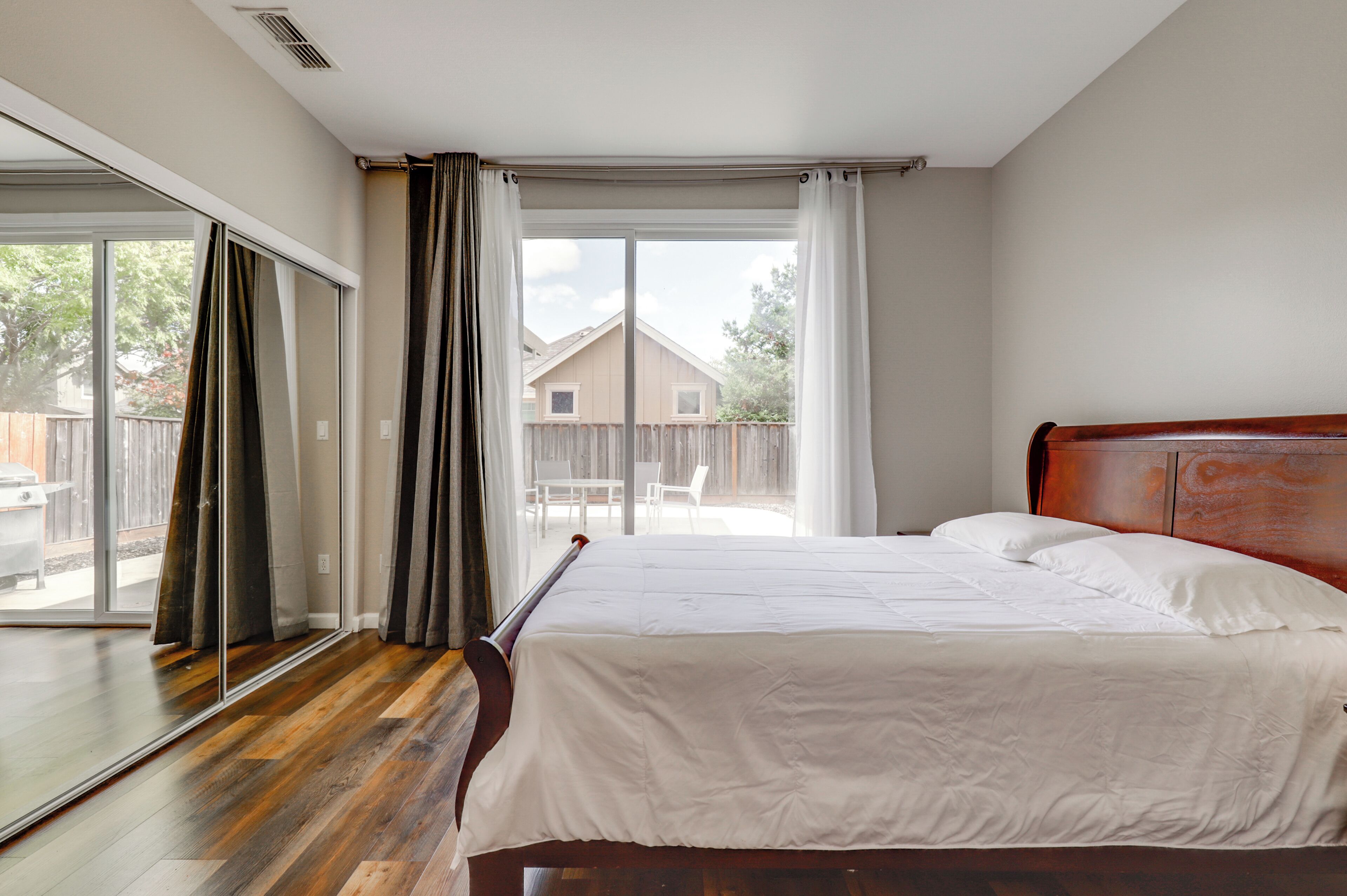 A bedroom with a large bed, a sliding glass door to a patio, and a view of a backyard.