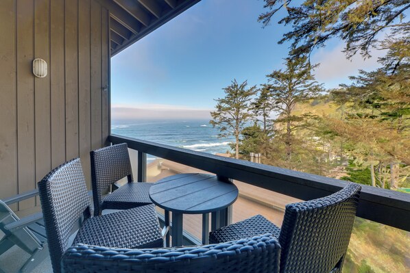 Un balcon meublé avec des meubles en osier, donnant sur une plage et l’océan.