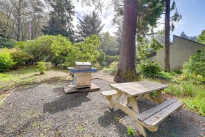 Un coin pique-nique aménagé avec un barbecue et une table dans une zone boisée.