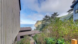 A wooden staircase leading to a building with a view of the ocean and hills. - Steps to Otter Crest Beach: Studio w/ Resort Perks (Newport)