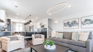 Uma sala de estar moderna com sofá, poltronas, uma mesa de centro com plantas e uma escada que leva a uma cozinha.