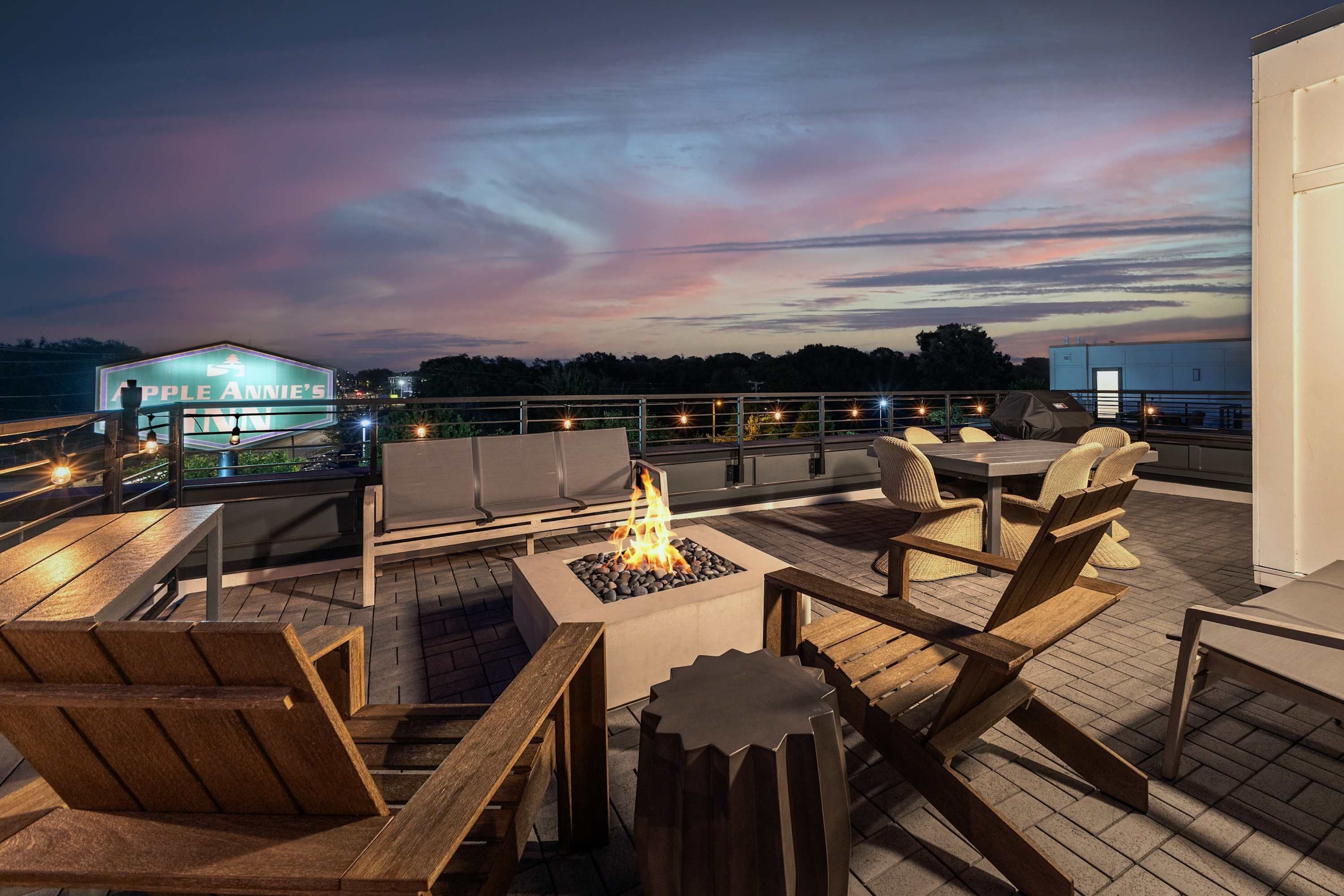 Een terras op het dak met buitenmeubilair, een vuurkorf en uitzicht op de skyline bij zonsondergang.