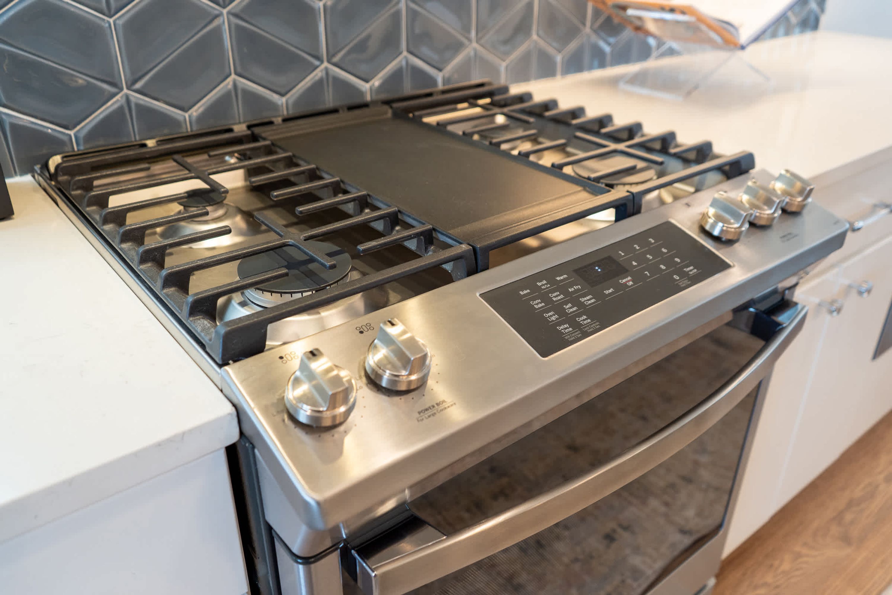 Une cuisine équipée d’une cuisinière, d’un four et d’un plan de travail en acier inoxydable, le mur derrière le plan de travail étant recouvert de carreaux.