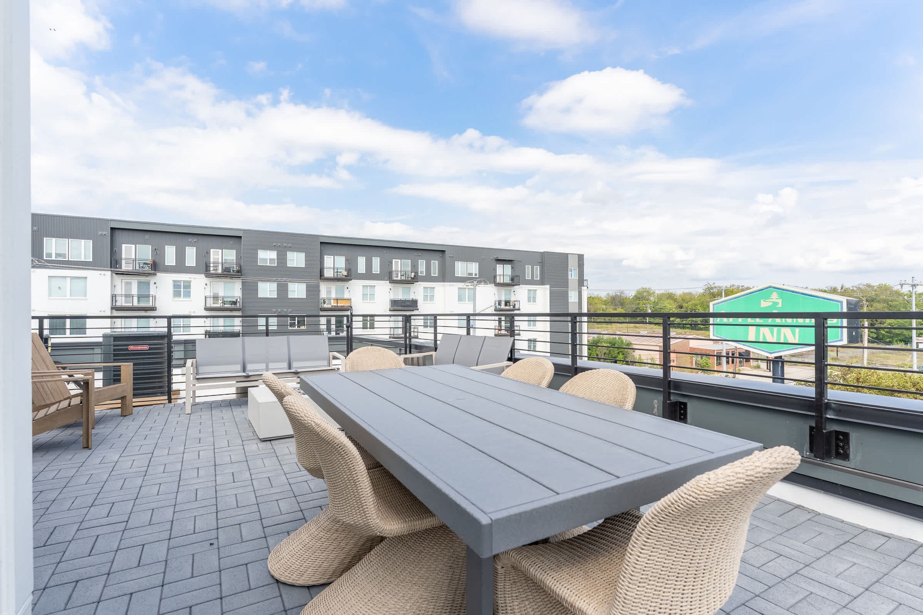 Une terrasse sur le toit, avec une table grise et des chaises en osier, d’où l’on peut admirer un bâtiment moderne et une enseigne verte.