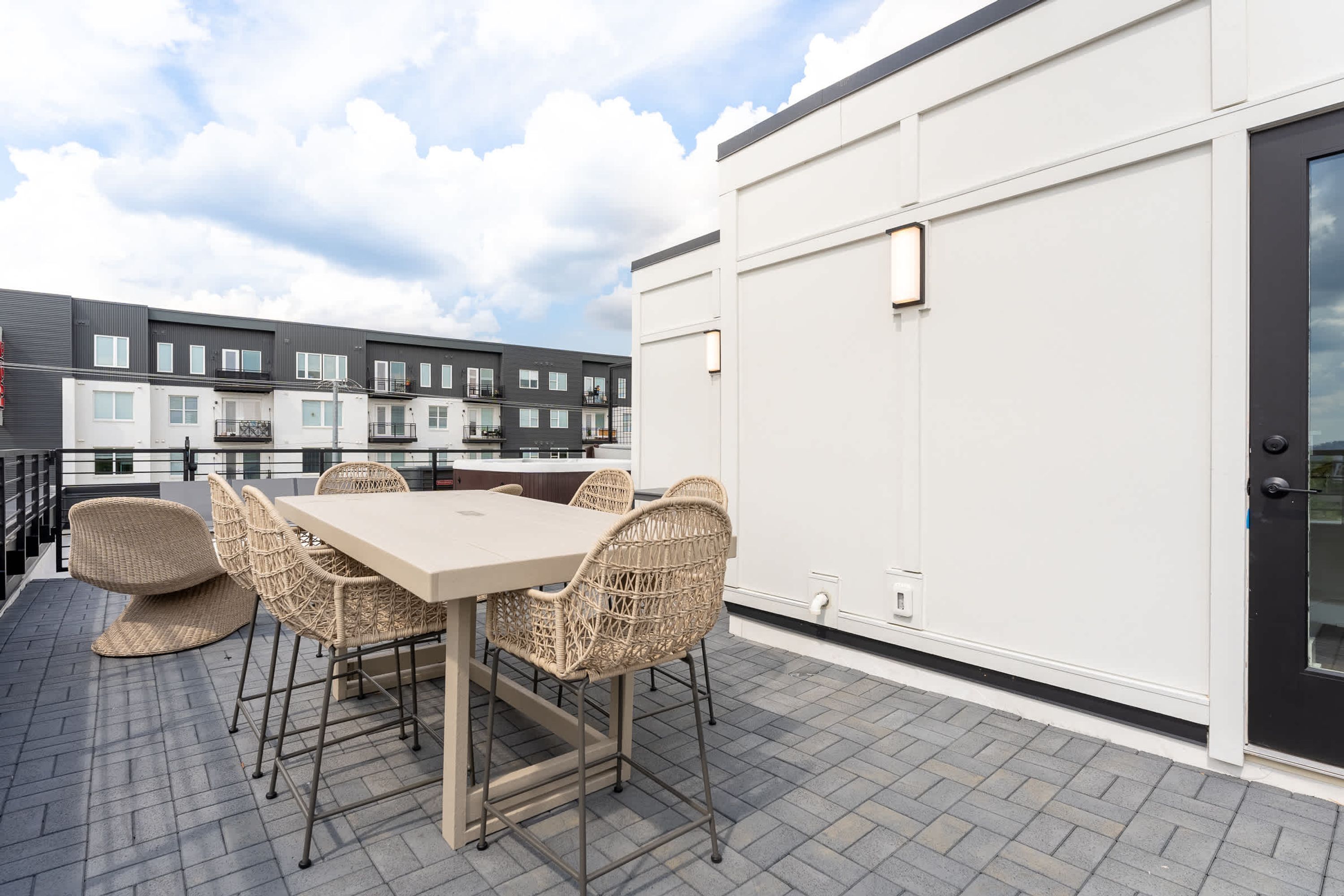 A rooftop terrace with a table and chairs, a view of neighboring buildings, and a door to the right.