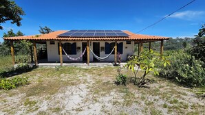 A house with a tiled roof, solar panels, and a hammock in front. - Camping Solar da Colina (Colinas do Sul)