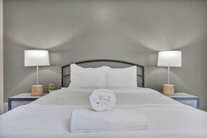 A neatly made bed with white linens and a rolled towel, flanked by two bedside tables with lamps and a small plant. - Location! Playhouse Sq ~ Fast Wi-Fi ~ Walkscore 96 (Cleveland)