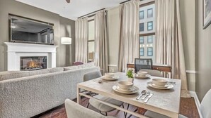 A modern living room with a fireplace, a dining area with a table set for four, and a large window with curtains. - Luxury Loft • Heart of Downtown• FREE Parking/Gym (Cleveland)