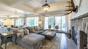 A spacious living room with a fireplace, large windows, and a chandelier.