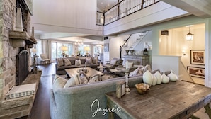 A spacious living area with a stone fireplace, a wooden dining table, and a high ceiling with exposed beams.