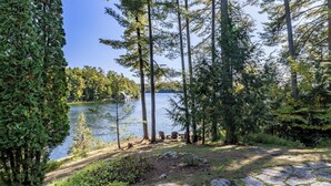 A lakeside view with stone steps leading to a seating area by the water, surrounded by trees.