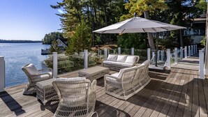 A wooden deck with wicker furniture and a large umbrella, overlooking a lake.