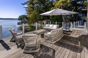 A wooden deck with wicker furniture and a large umbrella, overlooking a lake.