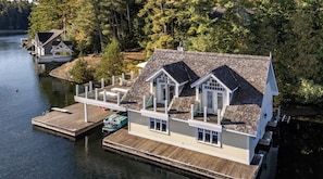 A houseboat with a dock, large windows, and a covered deck area. - Regal 9 bed 6 bath Cottage + Boathouse + Coachhouse on Lake Joe! (Parry Sound)