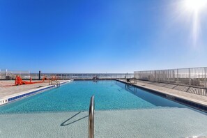 A clear blue pool with a 3 FT 6 IN depth marker, surrounded by a wooden deck and a metal railing, overlooking a beach.