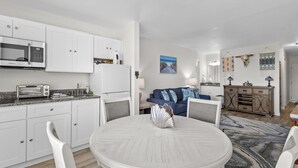 A modern kitchen with white cabinets, a microwave, and a toaster. There is a dining table with chairs and a decorative shell centerpiece.