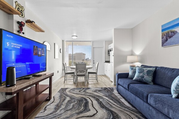 A modern living room with a large flat-screen TV, a blue sofa, and a marble-patterned rug.