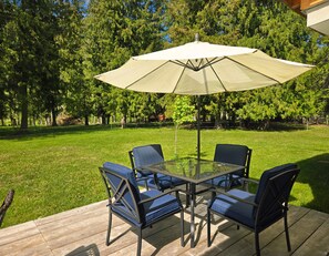 Un patio con mesa y sillas de vidrio, una sombrilla y una terraza de madera.