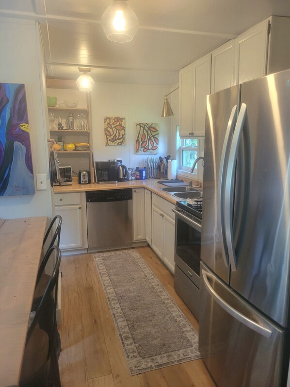 A modern kitchen with stainless steel appliances, wooden countertops, and a dining area with a table and chairs. - Peaceful Cedar Forest Guesthouse On Historic Farm (Creston)