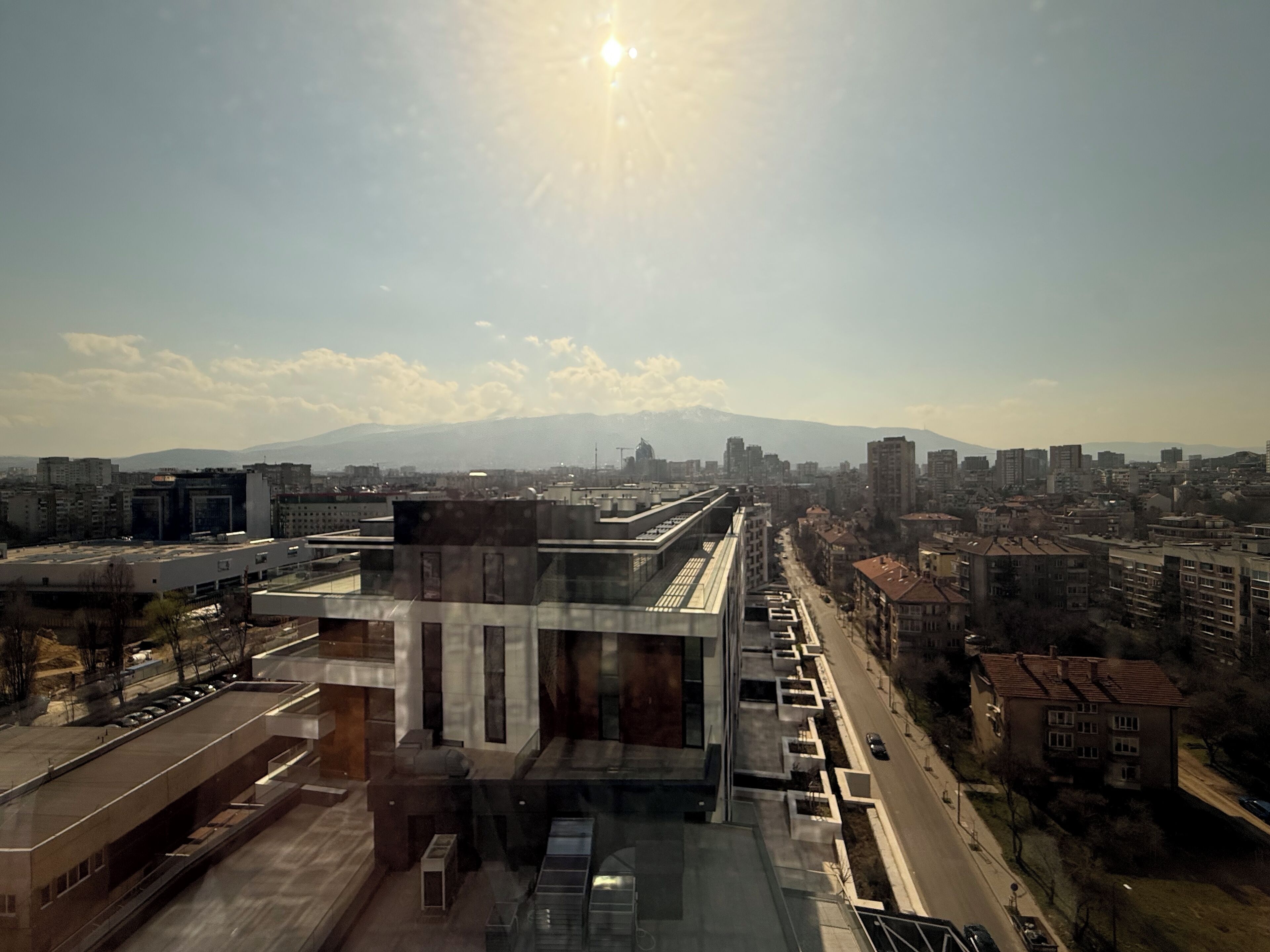 Un edificio moderno con fachada de vidrio, rodeado de construcciones urbanas y un cielo despejado.