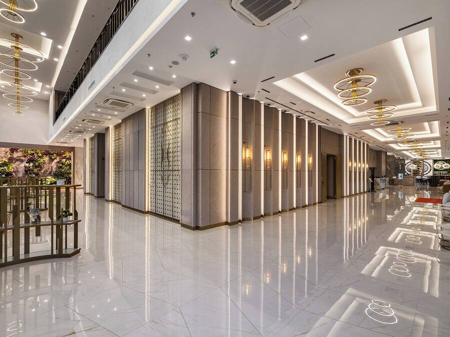 Un vestíbulo de hotel espacioso con piso pulido, luminarias modernas y una zona de estar con un muro decorativo de plantas.