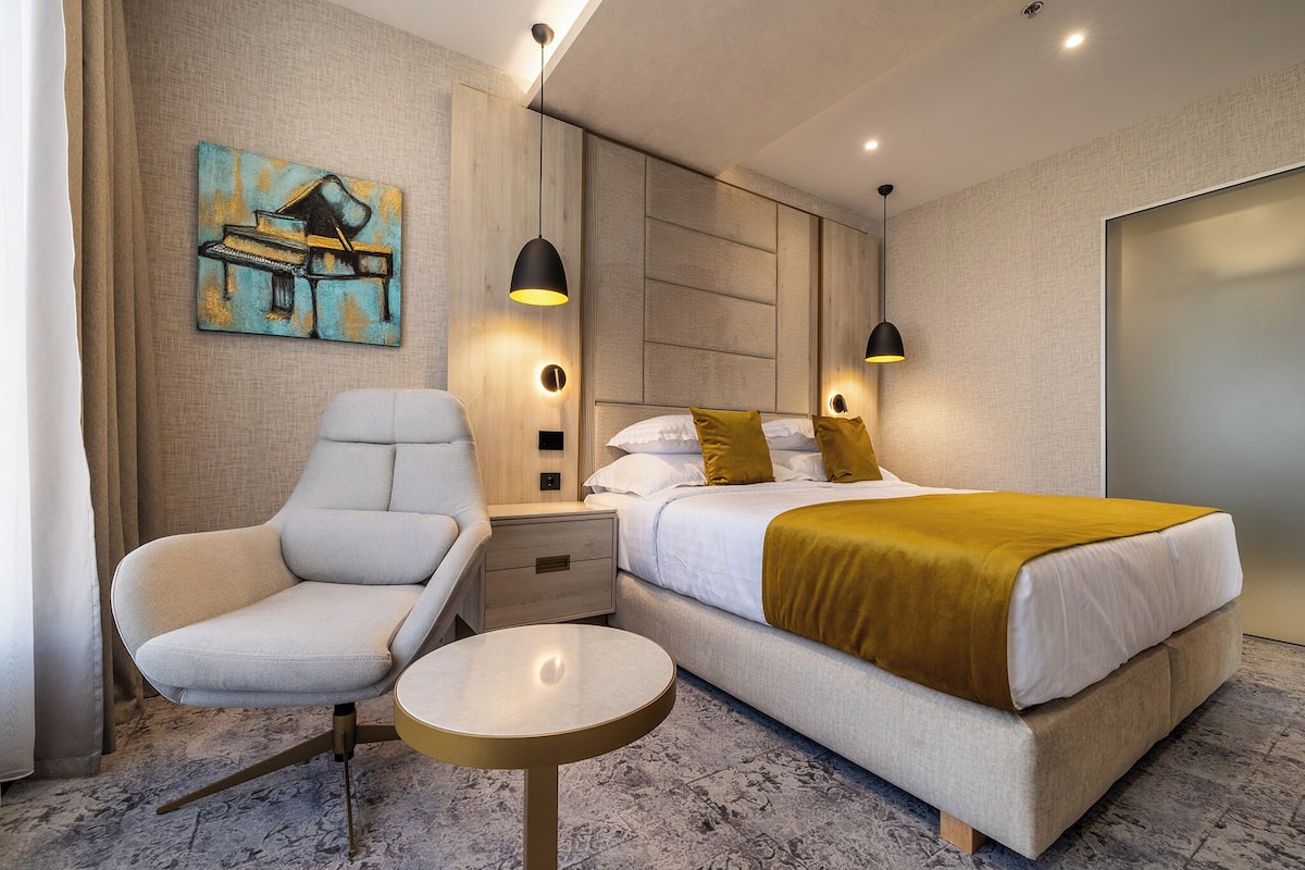 Une chambre d’hôtel moderne, équipée d’un lit, d’une chaise, d’une table de chevet et d’un tableau au mur.