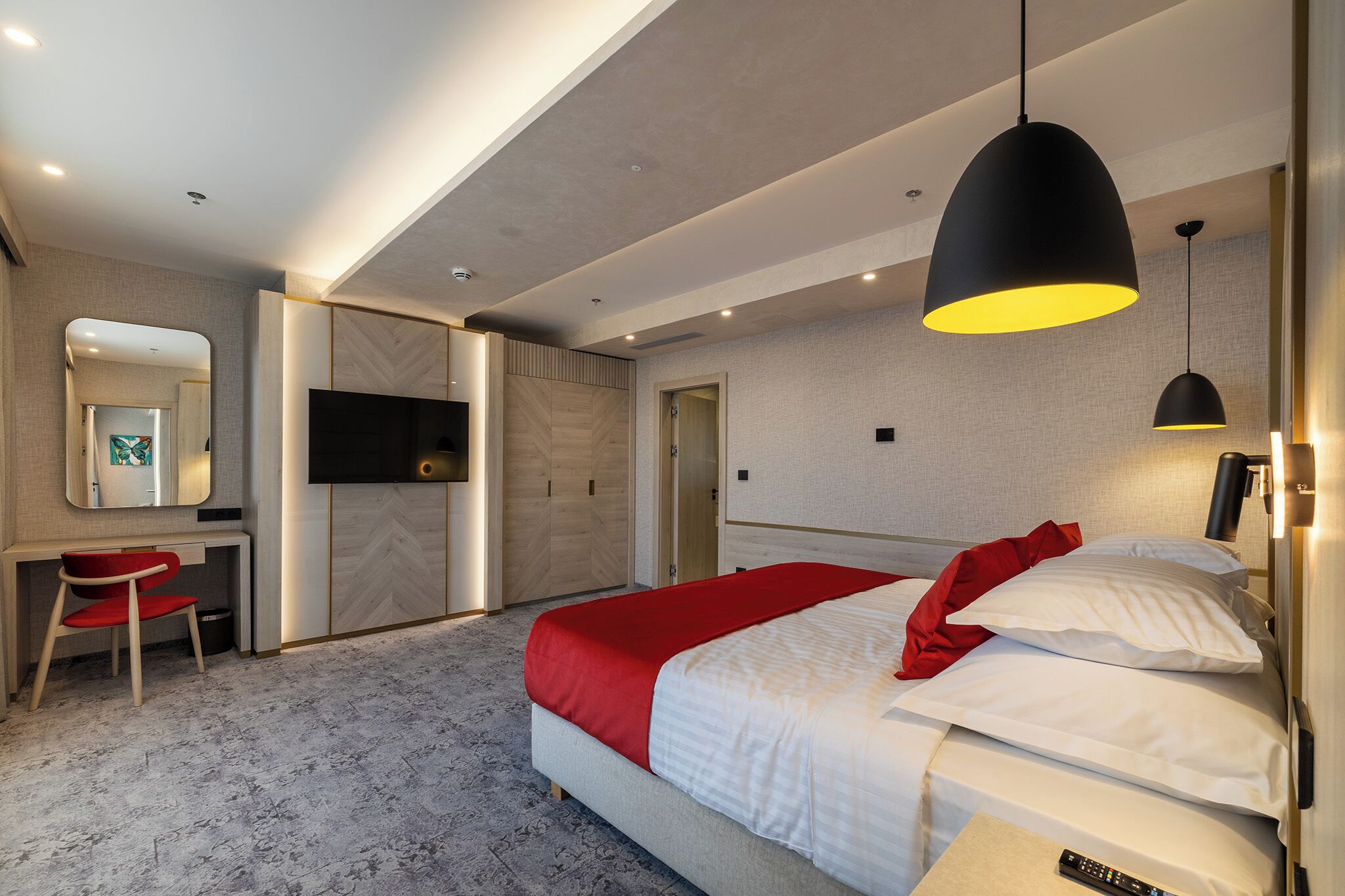 A modern hotel room with a bed, a desk, a chair, a TV, and a red blanket.