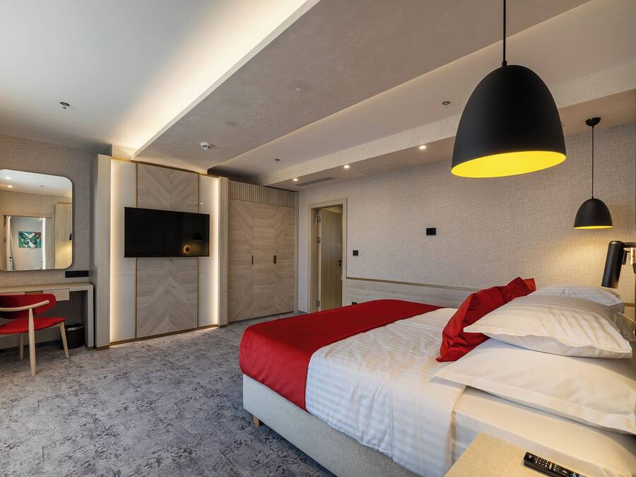 A modern hotel room with a bed, a desk, a chair, a TV, and a red blanket.