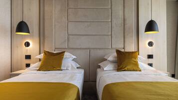 A hotel room with two beds, each with a headboard, a central wall panel, and two pendant lights.