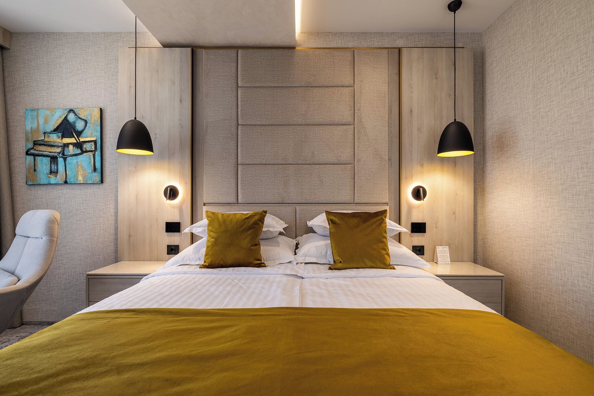 A modern hotel room with a large bed, two bedside tables, a chair, and a painting on the wall.