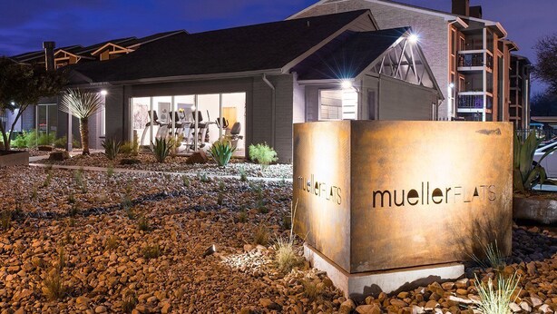 A modern building with a gym, a large sign reading 'Mueller Flats,' and a landscaped area with rocks and plants. - Sleepover | Peaceful 1BD/1BA + Gym - Austin TX (Austin)