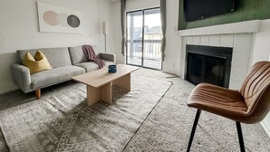 A living room with a sofa, coffee table, and armchair, a fireplace, and a TV mounted on the wall. - Sleepover | Peaceful 1BD/1BA + Gym - Austin TX (Austin)
