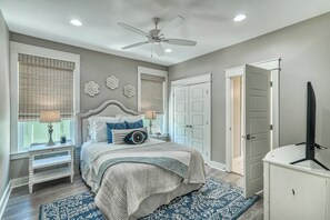 Un dormitorio con una cama, mesitas de noche, ventilador de techo y televisión.