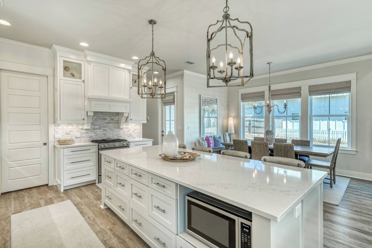 A modern kitchen with white cabinetry, a large island, a built-in microwave, and pendant lighting.