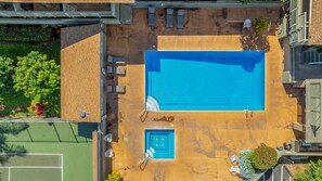 Vista aérea de una piscina con interior azul, rodeada de mobiliario exterior y un pequeño jardín.