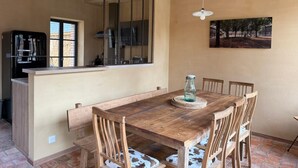 A dining area with a wooden table and chairs, a kitchen with a black refrigerator, and a window with a view of trees.