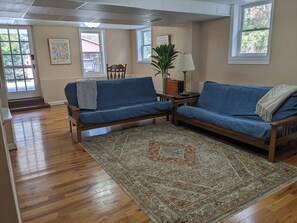 A living room with two blue sofas, a patterned rug, wooden flooring, and a window with a view of a building.