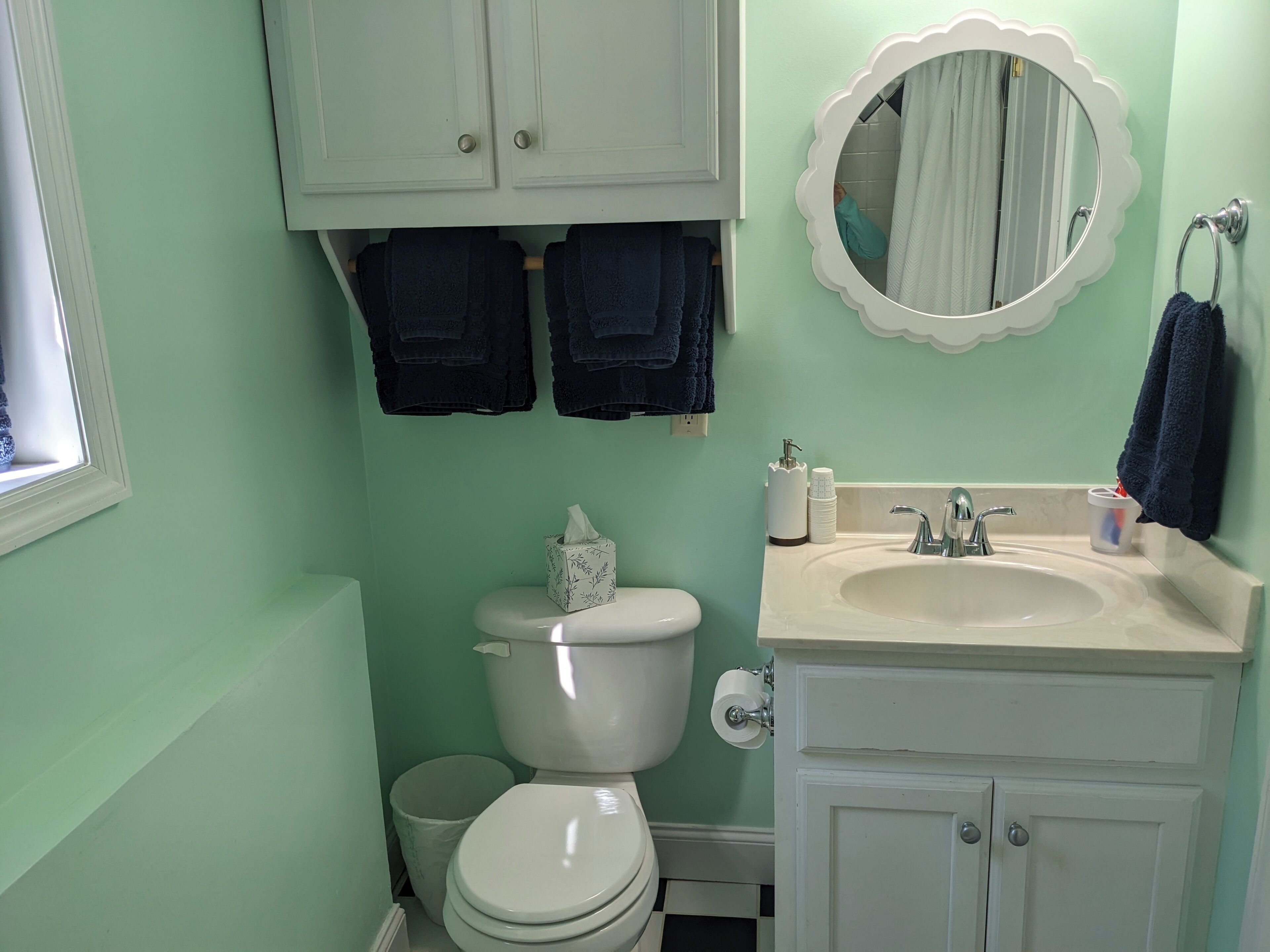 Een badkamer met toilet, wastafel en spiegel. Handdoeken hangen aan de muur en er staat een prullenbak.