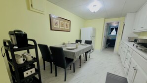 Een eetgedeelte met een tafel gedekt voor vier personen, stoelen, een koffieapparaat en een koelkast.