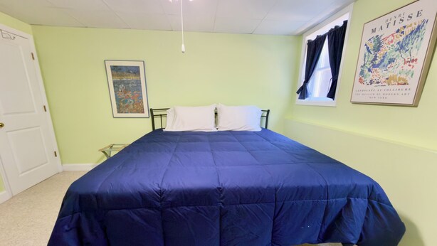 Een kamer met een bed, een deur, een raam met gordijnen en een schilderij aan de muur.