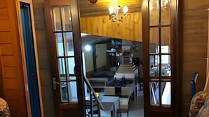 Een woonkamer met een bank, een bijzettafeltje en een kroonluchter. Er is een houten deur die leidt naar een keuken met een trap.