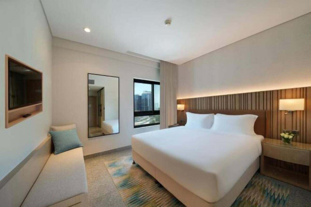 Une chambre d’hôtel avec un grand lit, une table de chevet, un miroir et une fenêtre.