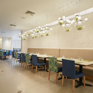 Un intérieur de restaurant moderne avec des banquettes, des tables rondes et des luminaires sphériques suspendus, agrémentés de plantes.