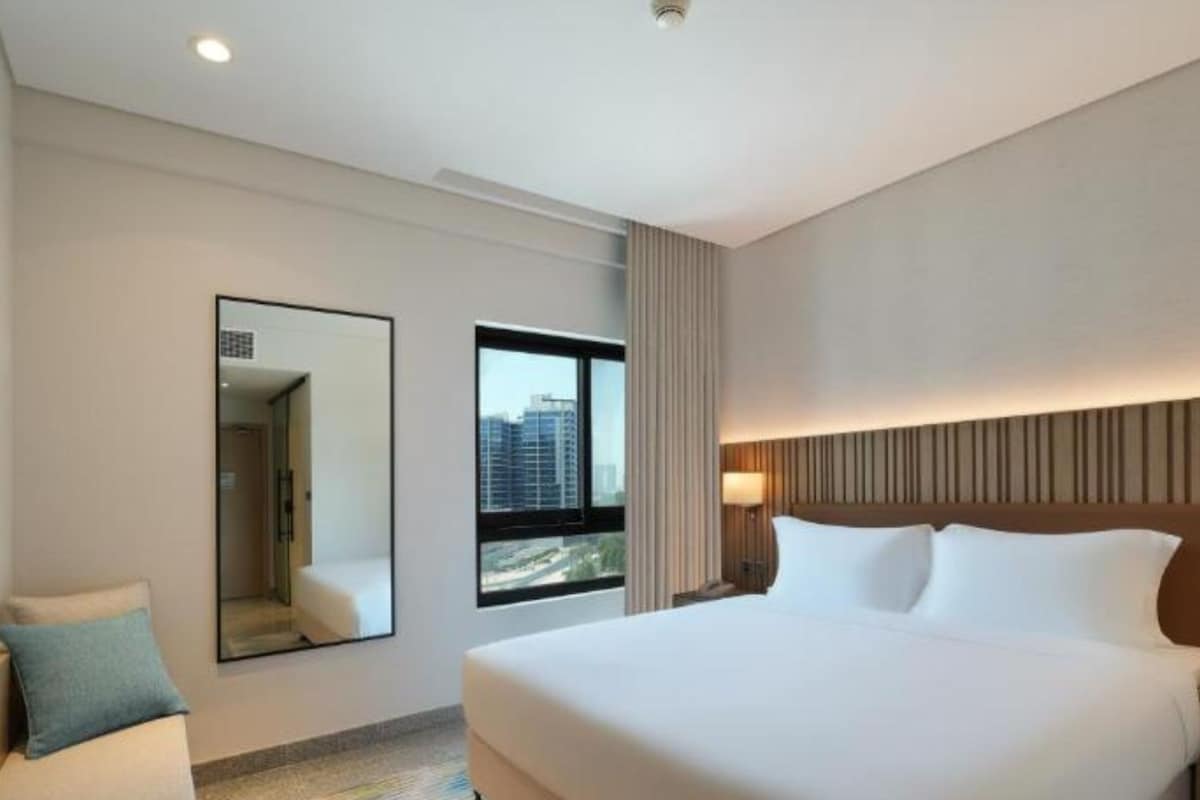 Une chambre d’hôtel avec un grand lit, un miroir, une fenêtre donnant sur la ville et un luminaire au plafond.