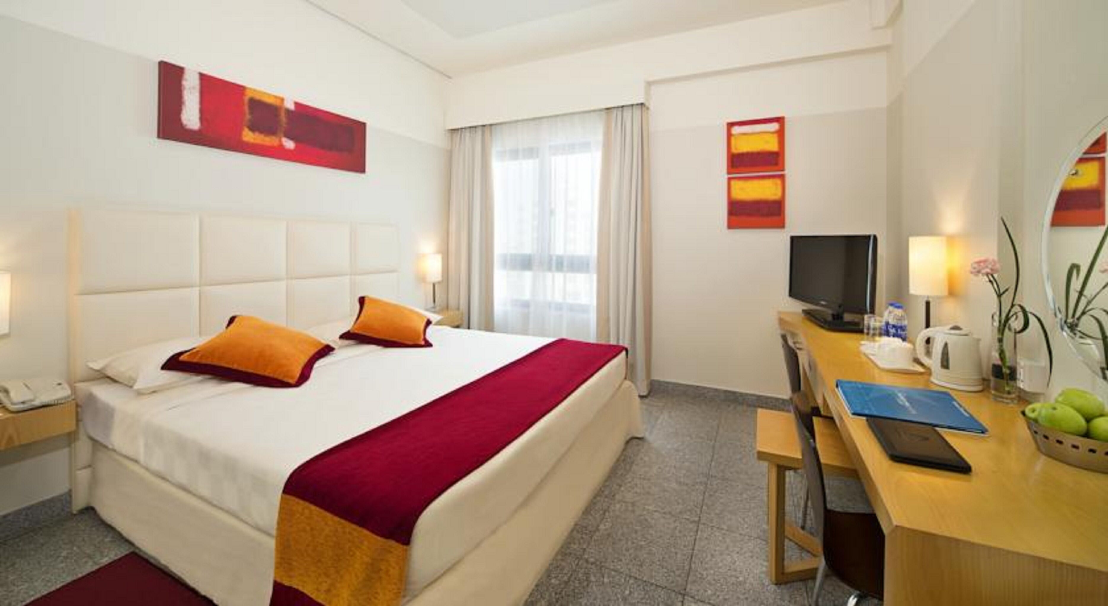 A hotel room with a bed, a desk, a television, and a window with curtains.